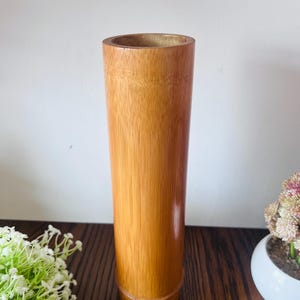 May include: A tall, cylindrical vase crafted from natural bamboo with a smooth, polished finish. The vase features the characteristic vertical grain and light brown colour of bamboo, with a single horizontal node ring near the base.