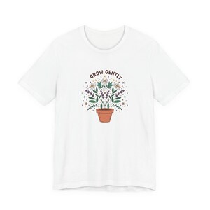 Puede incluir: Una taza de cerámica blanca con un asa negra y el texto "But First, Coffee" en negrita negra. La taza está sobre una superficie de madera. La taza mide aproximadamente 10 cm de altura.