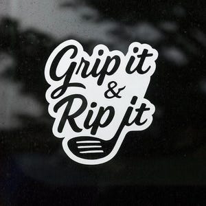 May include: White sticker with the text "Grip it & Rip it" in a stylized font, accompanied by a golf club graphic. The sticker is designed to be applied to a car window or similar surface.