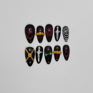 Pode incluir: Um conjunto de dez unhas postiças pretas com vários desenhos. Os desenhos incluem detalhes em vermelho e dourado, uma espada prateada e uma espiral em preto e branco. As unhas são ovais e têm um acabamento brilhante.