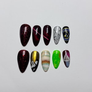 May include: A set of ten almond-shaped press-on nails featuring diverse designs including deep red glitter, cat-eye effects, silver geometric lines, a circular emblem with the text "HAIL EARTH", gold metallic accents, marble swirls, and neon green.