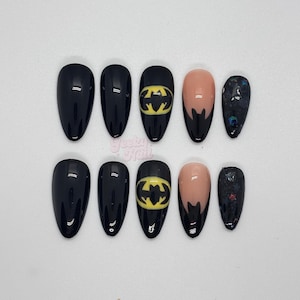 Pode incluir: Um conjunto de dez unhas postiças pretas em forma de amêndoa. Duas unhas apresentam o logotipo do Batman em amarelo. Duas unhas têm uma base nude com pontas pretas. Uma unha tem um design de glitter escuro. As unhas estão dispostas sobre uma superfície branca.