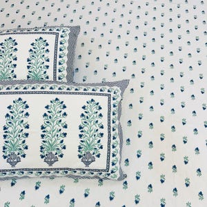 May include: White bedsheets and pillowcases with a blue and green floral pattern. The pillowcases have a border with a blue and white striped design. The sheets have a repeating pattern of small blue flowers.