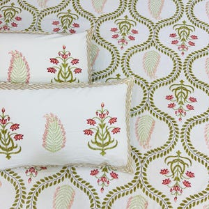 May include: White pillowcases and a patterned sheet set with a floral design. The pillowcases have a gold trim and feature embroidered pink and green floral motifs. The sheet set has a repeating green leaf pattern with pink accents.