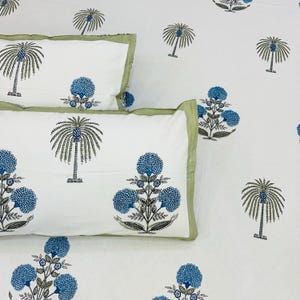 May include: White bedding set with a repeating pattern of blue floral and palm tree designs. The pillowcases have a green border. The overall design is a tropical theme.