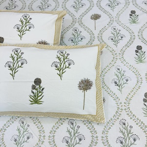 May include: White bedding set with a floral pattern. The set includes two pillowcases and a sheet, all featuring green and black floral designs. The pillowcases have a tan striped border. The sheet has a repeating floral pattern.