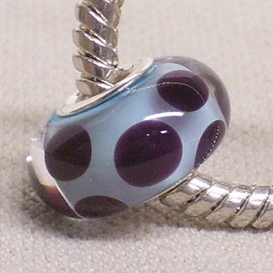 May include: A silver charm bracelet with a light blue glass bead with purple polka dots.