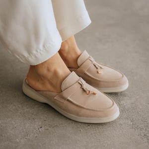 Beige suede loafer mules with tassels and open back on white background