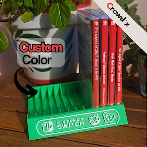 May include: A bright green plastic Nintendo Switch game storage rack with multiple slots. The front features the white Nintendo Switch logo and two character icons. Four game cases are inserted into the rack, including titles like The Legend of Zelda: Breath of the Wild, Pokémon Diamante Brillante, and Super Mario Bros. Wonder.