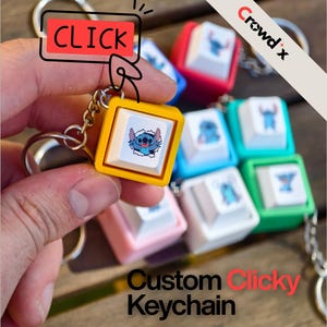 Può includere: Una collezione di portachiavi colorati a forma di tasti della tastiera, con immagini di personaggi dei cartoni animati. I portachiavi sono quadrati e stampati. È visibile anche il testo "CLICK" e "Custom Clicky Keychain".