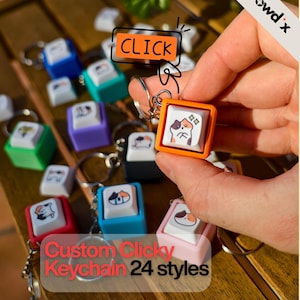 Peut inclure: Porte-clés clicky personnalisés en 24 styles. Les porte-clés présentent des touches carrées colorées avec des illustrations de chats. Les touches sont fixées à des porte-clés. L'image comprend le mot "CLICK" dans un encadré orange.