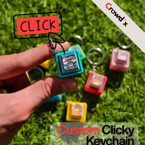 Puede incluir: Una mano sostiene un llavero clicky cuadrado turquesa con un gráfico de dibujos animados. Se ven otros llaveros de colores, amarillos, verdes y rosas. La imagen incluye el texto "CLICK" y "Custom Clicky Keychain".