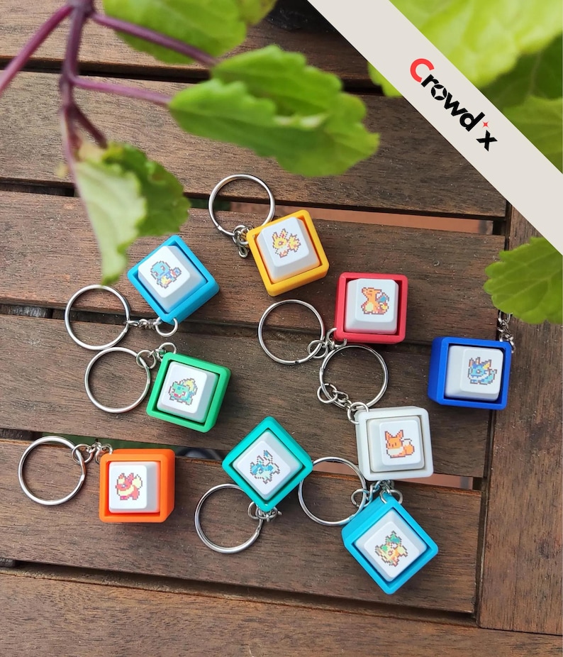 K&ouml;nnte beinhalten: Eine Sammlung farbenfroher Schl&uuml;sselanh&auml;nger mit quadratischen Tastenkappen mit Cartoon-Charakter-Designs. Jeder Schl&uuml;sselanh&auml;nger hat einen silbernen Ring und einen andersfarbigen Rahmen, darunter Blau, Gelb, Rot und Gr&uuml;n. Der Text "Crowd x" ist sichtbar.
