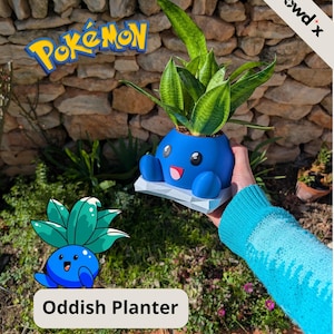 Può includere: Un vaso Oddish blu con una faccia sorridente, che contiene una pianta verde. Il vaso è su una base bianca. L'immagine include il testo "Pokemon" e "Oddish Planter".