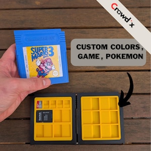 May include: A blue Nintendo Game Boy cartridge labeled "Super Mario 3" is held above a black and yellow storage case. The case has multiple compartments for game cartridges and SD cards. Text on the image reads "CUSTOM COLORS, GAME, POKEMON."