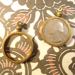 May include: Two brass coin frames, one with a silver quarter inside. The quarter is dated 1976 and features the profile of George Washington. The frames have a decorative edge and a loop at the top for hanging.