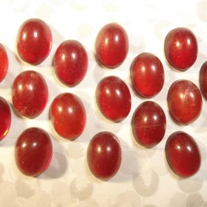 Puede incluir: Una colección de 17 cabujones ovalados de vidrio rojo. Los cabujones son lisos y brillantes.