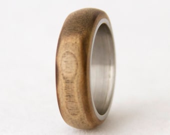 May include: A wooden ring with a silver band. The wood is a light brown color and has a natural grain pattern. The silver band is polished and shiny.