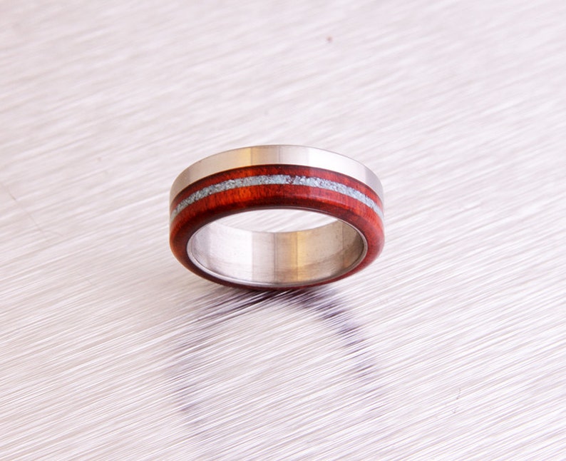 May include: A stainless steel ring with a band of dark red wood and two thin silver lines.