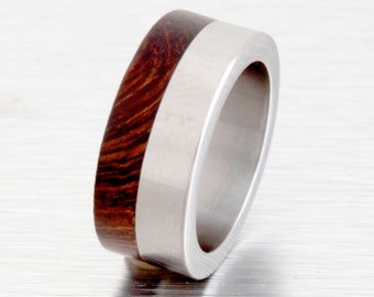 May include: A silver and brown wood ring. The ring is made of stainless steel and has a band of wood on one side.