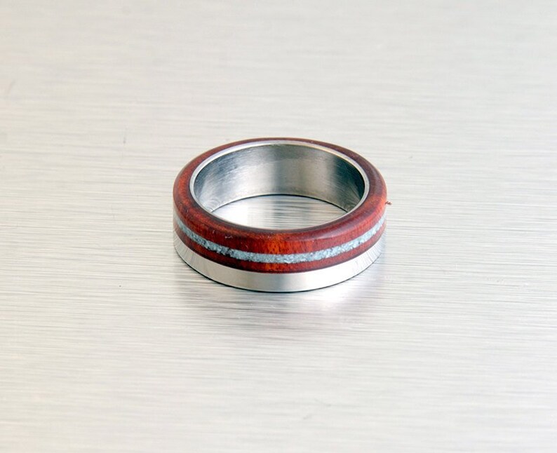 May include: A stainless steel ring with a band of red wood and a thin silver inlay.
