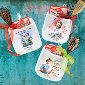 May include: Three white oven mitts with retro nurse graphics and text, each holding a Betty Crocker baking mix. One says "When the squad looks better in scrubs", another "I love how we don't have to say out loud that I'm your favorite nurse", and the third "Nurse Practitioner".