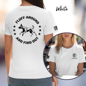 May include: White t-shirt with a black graphic of a dog and the text "FLUFF AROUND AND FIND OUT". The shirt also features a small American flag on the sleeve and the text "White" in cursive.