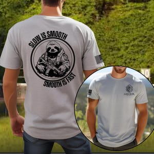 May include: Light gray t-shirt with a black graphic of a sloth holding a rifle, encircled by the text "SLOW IS SMOOTH, SMOOTH IS FAST." An American flag is on the sleeve. A smaller image shows the shirt with a lion logo.