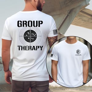 May include: White t-shirt with the words "GROUP THERAPY" above and below a target graphic. The shirt also features a small American flag on the sleeve and a logo on the other side.