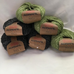Könnte beinhalten: Mehrere Wollknäuel in Grün- und Grautönen. Jedes Knäuel hat ein braunes Etikett mit dem Text "ADRIAFIL WoCa". Das Garn scheint weich zu sein, ideal für Strick- oder Häkelprojekte. Das Bild ist gut beleuchtet.