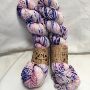 Può includere: Due matasse di filato tinto a mano nei toni del rosa, bianco e blu. Il filato è etichettato "kenya" e "Stratus DK". Il filato è una fibra morbida e strutturata, perfetta per progetti di maglia o uncinetto.
