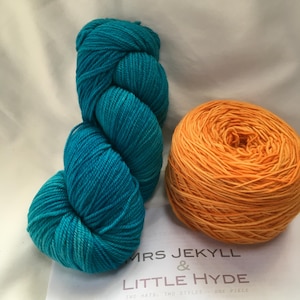 Puede incluir: Primer plano de dos madejas de hilo. Una es de color turquesa vibrante y la otra de color naranja brillante. El hilo turquesa tiene forma de trenza retorcida, mientras que el hilo naranja tiene forma de bola redonda. El texto "MRS JEKYLL & LITTLE HYDE" es visible.