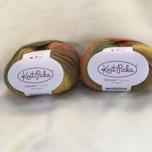 Può includere: Due gomitoli di filato Knit Picks Chroma Worsted. Il filato è un mix di colori verdi, gialli, arancioni e marroni. Ogni gomitolo ha un'etichetta bianca con il logo Knit Picks e informazioni.