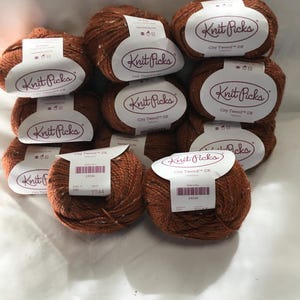 Può includere: Una collezione di gomitoli di lana marrone con etichette bianche. Le etichette riportano "Knit Picks City Tweed DK". La lana è di colore marrone screziato. Le etichette contengono anche un codice a barre e altre informazioni.