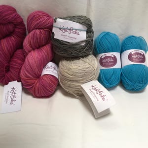 Può includere: Una collezione di gomitoli di filato in vari colori, tra cui tonalità di rosa, verde acqua, grigio e beige. Il filato è etichettato con il marchio "Knit Picks". L'immagine mostra diverse trame e pesi di filato, adatti per progetti di maglieria e uncinetto.