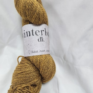 Pode incluir: Uma bola de fio amarelo mostarda com um rótulo branco que diz "winterbul dk baa ram ewe".