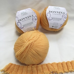 May include: Three skeins of yellow DONNINA Fine Italian-Style Merino wool yarn with labels, and a knitted swatch. The yarn is a soft, light yellow color. The labels have the brand name and product details.