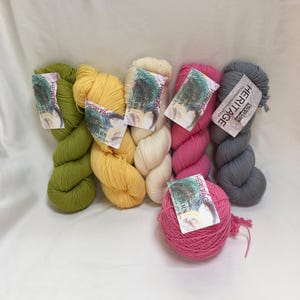 May include: A collection of colorful yarn skeins and a ball of yarn. The yarn colors include green, yellow, cream, pink, and gray. Each skein has a tag with the word "HERITAGE" on it. The yarn is arranged on a white surface.