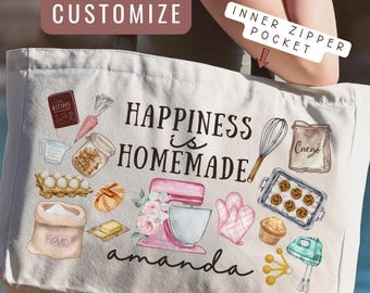 May include: A white canvas tote bag featuring the text "HAPPINESS is HOMEMADE" and the name "amanda" in black script. The design includes colorful illustrations of baking supplies like a pink stand mixer, whisk, flour bag, and cookies.