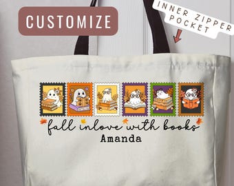May include: A cream-coloured canvas tote bag with black handles and an inner zipper pocket. The front features six colourful stamp-style illustrations of ghosts reading books, the text "fall inlove with books", and the personalised name "Amanda".