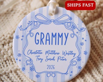 May include: A round, white ceramic ornament with light blue vertical stripes and a blue decorative frame. The text reads GRAMMY, followed by the names Charlotte, Matthew, Westley, Troy, Sarah, Peter, and the year 2026, accented by blue snowflakes.