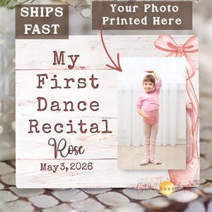 May include: A personalized wooden plaque with a photo of a young girl in a pink leotard, with the text "My First Dance Recital Rose May 3, 2026". The plaque has a rustic, white-washed wood background.