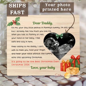 May include: Wooden plaque with a heart-shaped sonogram image, a green bow, and text that reads "Dear Daddy." The plaque includes Christmas-themed illustrations and the text "It's going to be the Best Christmas Ever! Christmas 2026."