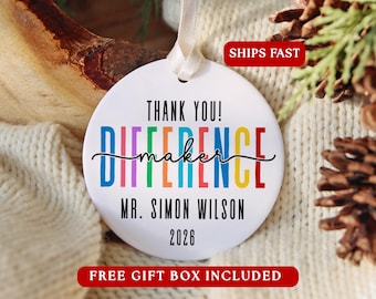 May include: A round white ceramic ornament with a cream-coloured ribbon hanger. The text reads THANK YOU! in black, followed by the word DIFFERENCE in multicoloured letters, with maker in black script, MR. SIMON WILSON, and the year 2026.