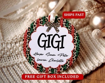 May include: A round ceramic ornament featuring a leopard print and red and green striped background. A white scalloped centre displays the name GIGI in black text, with the names Harper, Simon, Peter, Lauren, and Charlotte below.