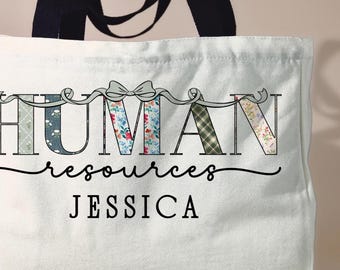 May include: A white canvas tote bag with black handles featuring the text HUMAN RESOURCES in block letters filled with various floral and plaid patterns, a grey bow graphic, the word resources in script, and the name JESSICA in black text.
