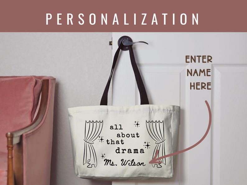 May include: Cream-colored tote bag with black handles, hanging on a white door. The bag features the text "all about that drama" with a name below, and illustrations of theater curtains. The word "PERSONALIZATION" is at the top.
