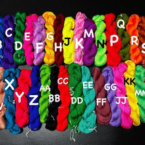 May include: A collection of colorful yarn skeins labeled with letters from A to Z. The yarn is arranged in two rows, with the first row starting with A and ending with T, and the second row starting with U and ending with PP.