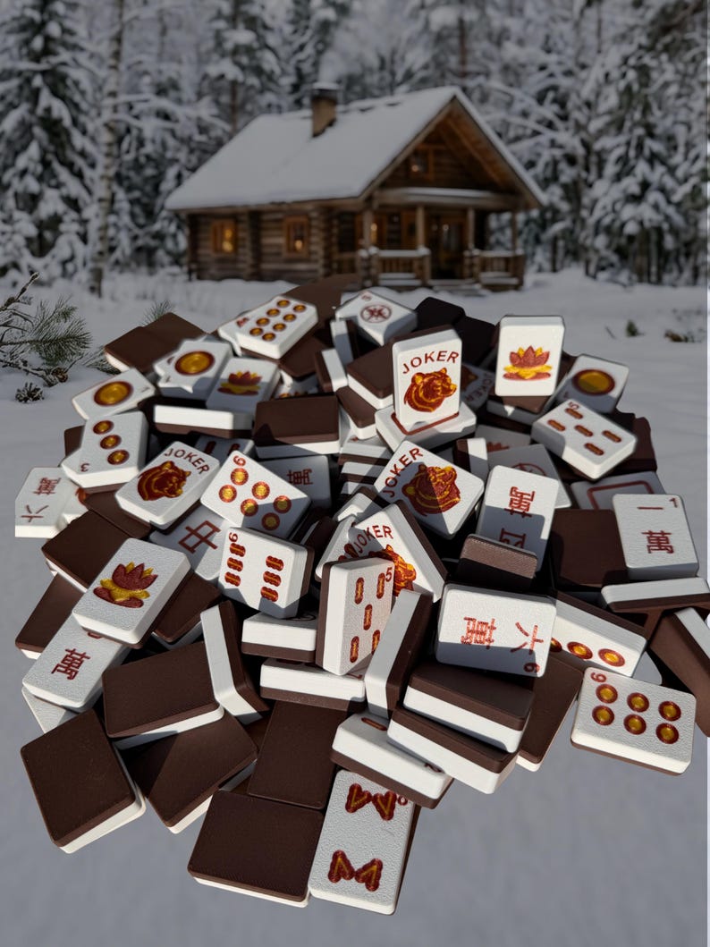 May include: A pile of Mahjong tiles with brown backs and white faces, featuring various symbols and characters. Some tiles display the word "JOKER" and other Chinese characters. The game pieces are scattered on a snowy surface.