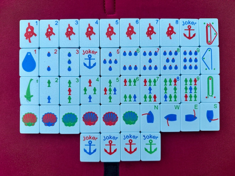May include: A collection of white Mahjong tiles with various symbols and numbers in red, blue, green, and black. The tiles feature anchors, water droplets, and other designs. Several "Joker" tiles are also present, along with directional tiles.
